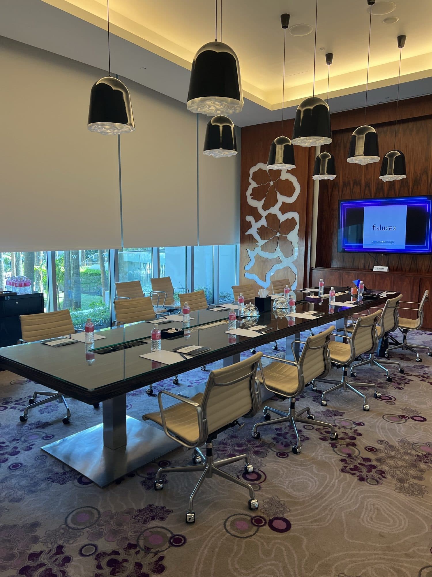 An empty boardroom set for a Flyluxex meeting, with a city view through floor to ceiling windows