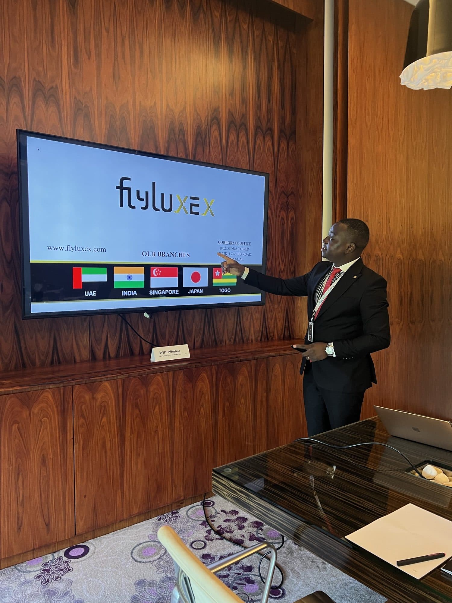 A Flyluxex representative presenting the firm's branch network on screen in a wood-panelled boardroom