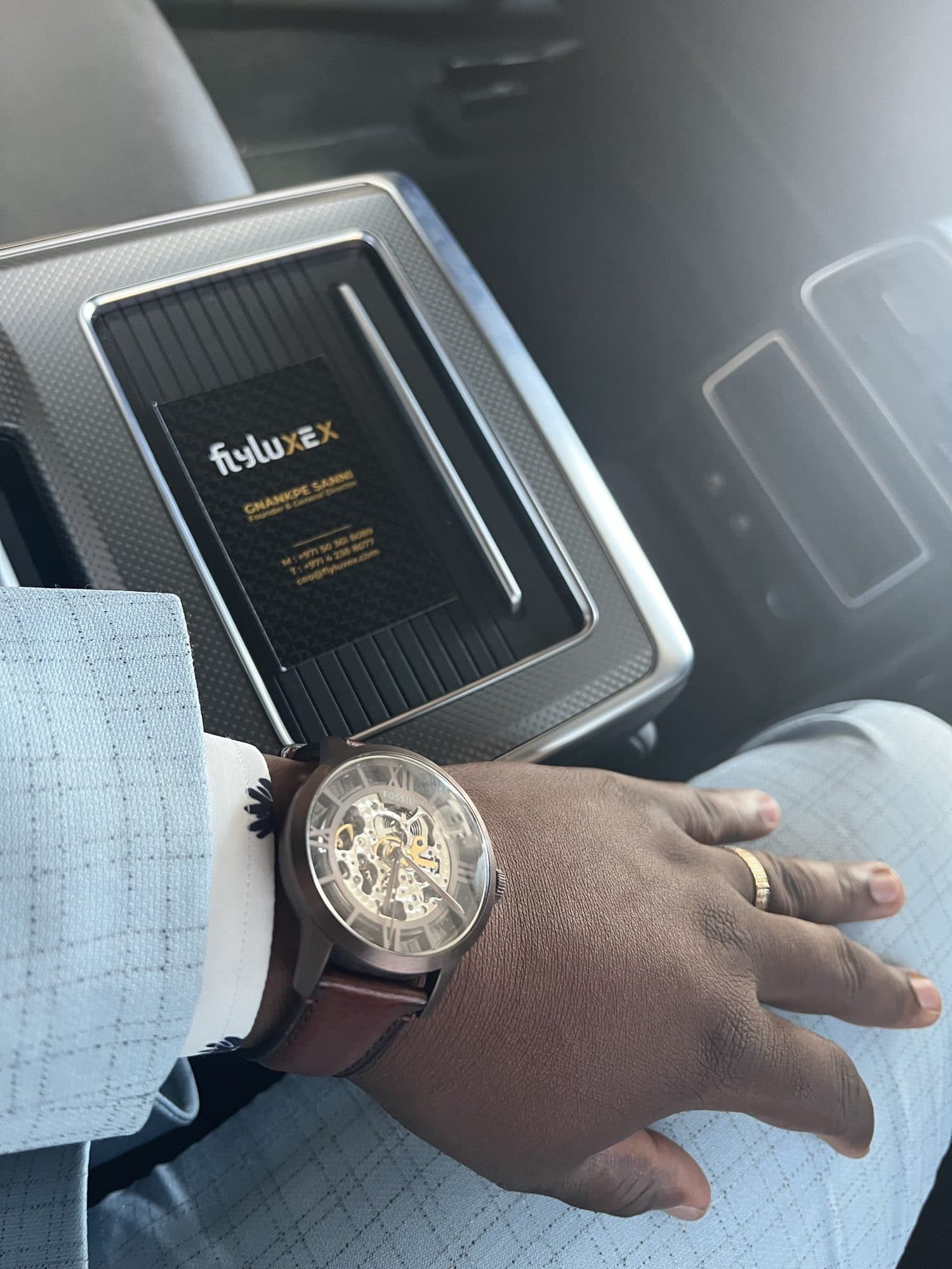 A Flyluxex business card and wristwatch, photographed inside a private car