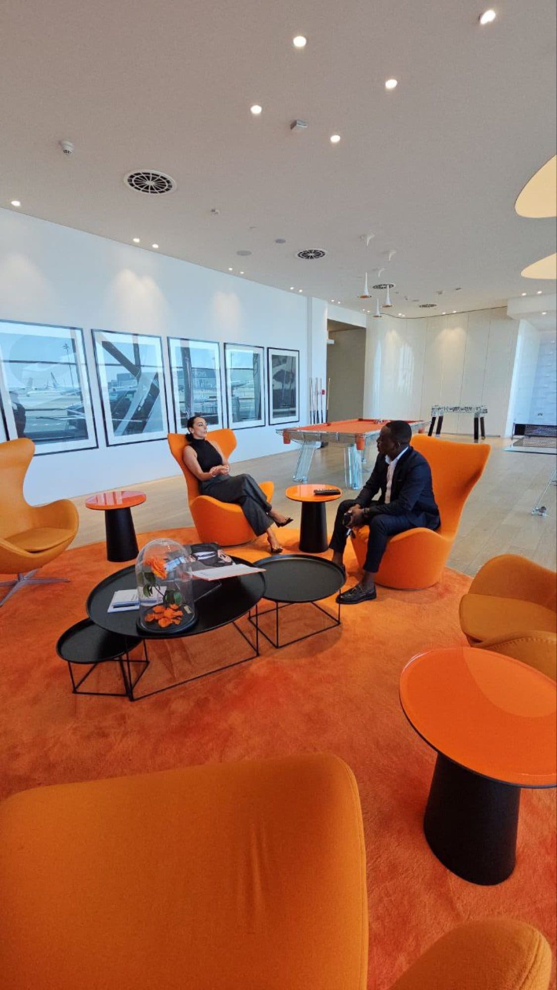 Two colleagues in conversation in the Flyluxex lounge, seated in a pair of orange armchairs