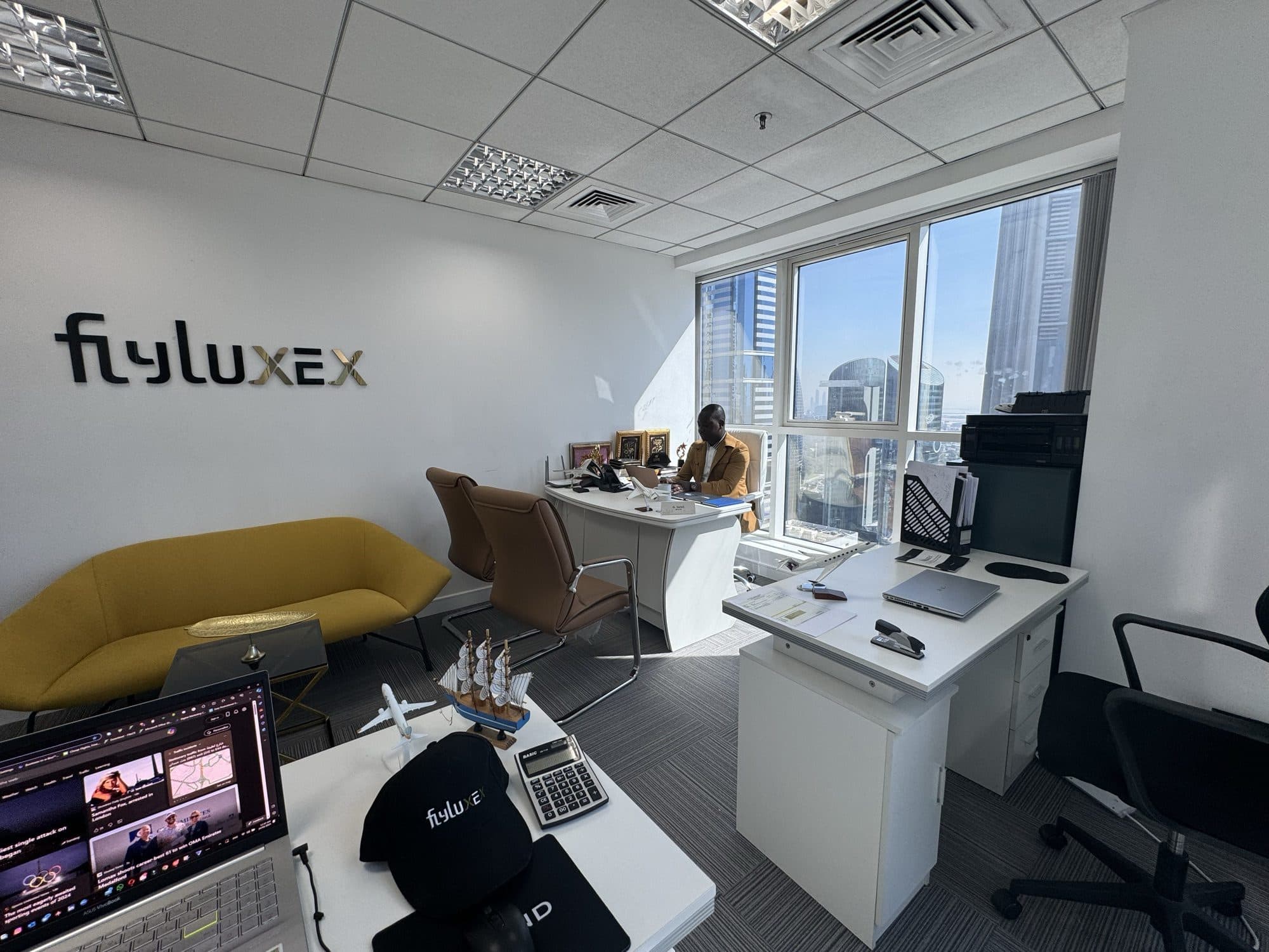 A Flyluxex team member at his desk, with Dubai's skyline framed by the office window
